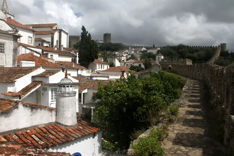 Caminho de ronda da muralha de Óbidos em curva até ao castelo, com os telhados da vila